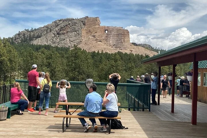 Touristen entspannen und fotografieren auf einer Holzterrasse mit Bergblick.