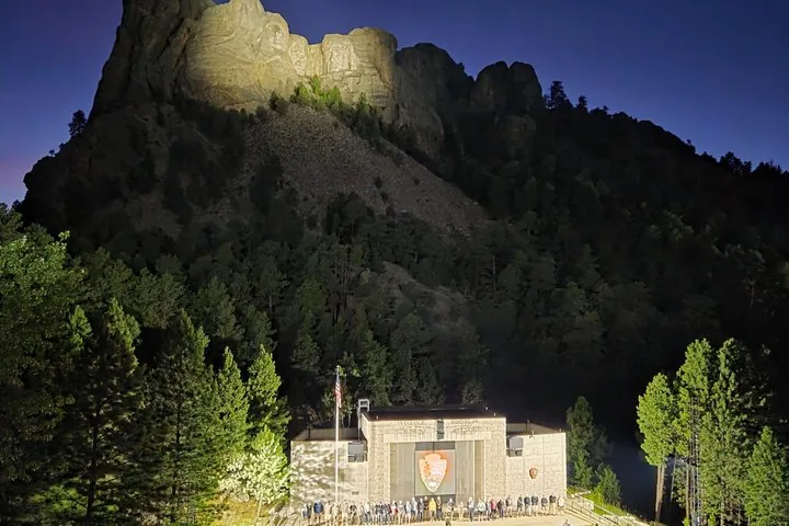 Vista panorámica nocturna del Monte Rushmore iluminado y el anfiteatro al aire libre.