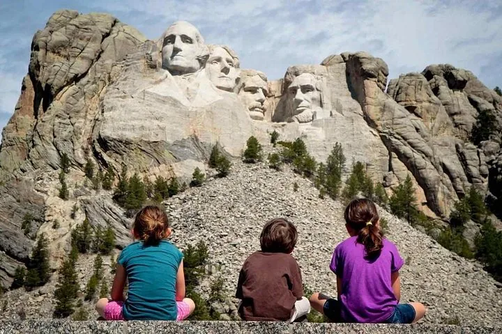Tres niños sentados en una repisa, admirando las esculturas del Monte Rushmore.